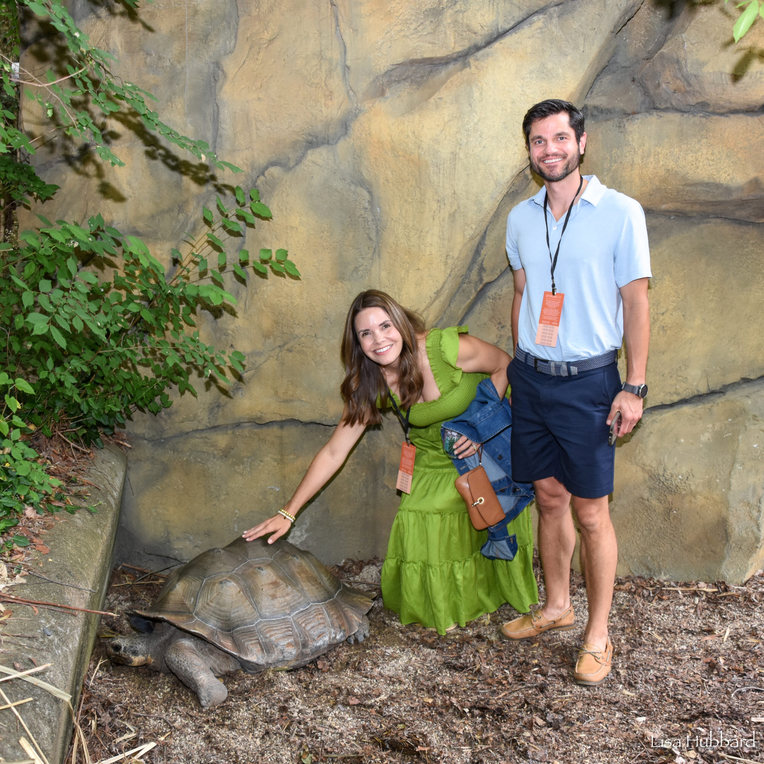a man and woman posing with a galapagos tortoise at a zoo event