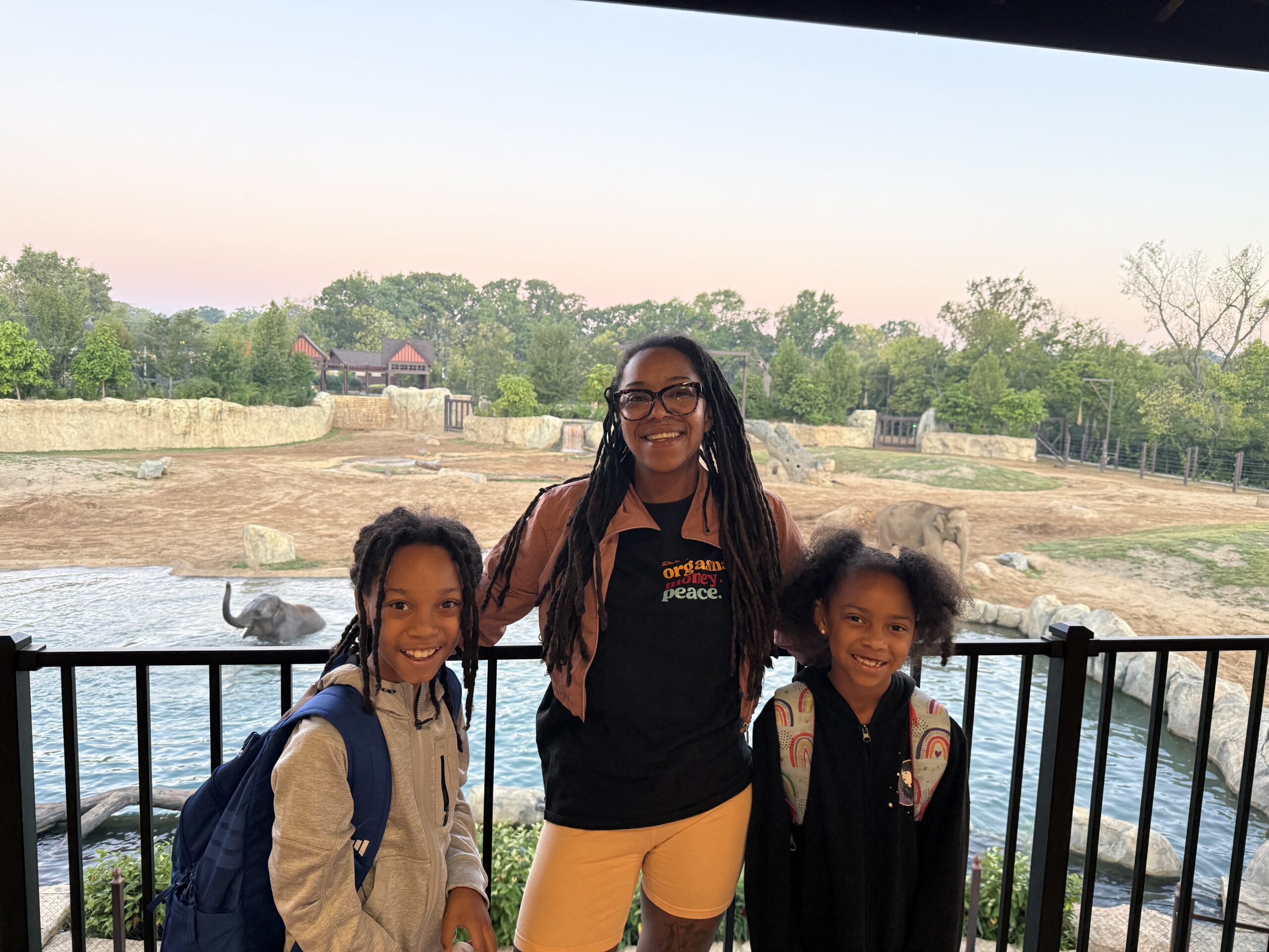 and adult and two little girls posing in front of the elephant trek pool with elephant in the water