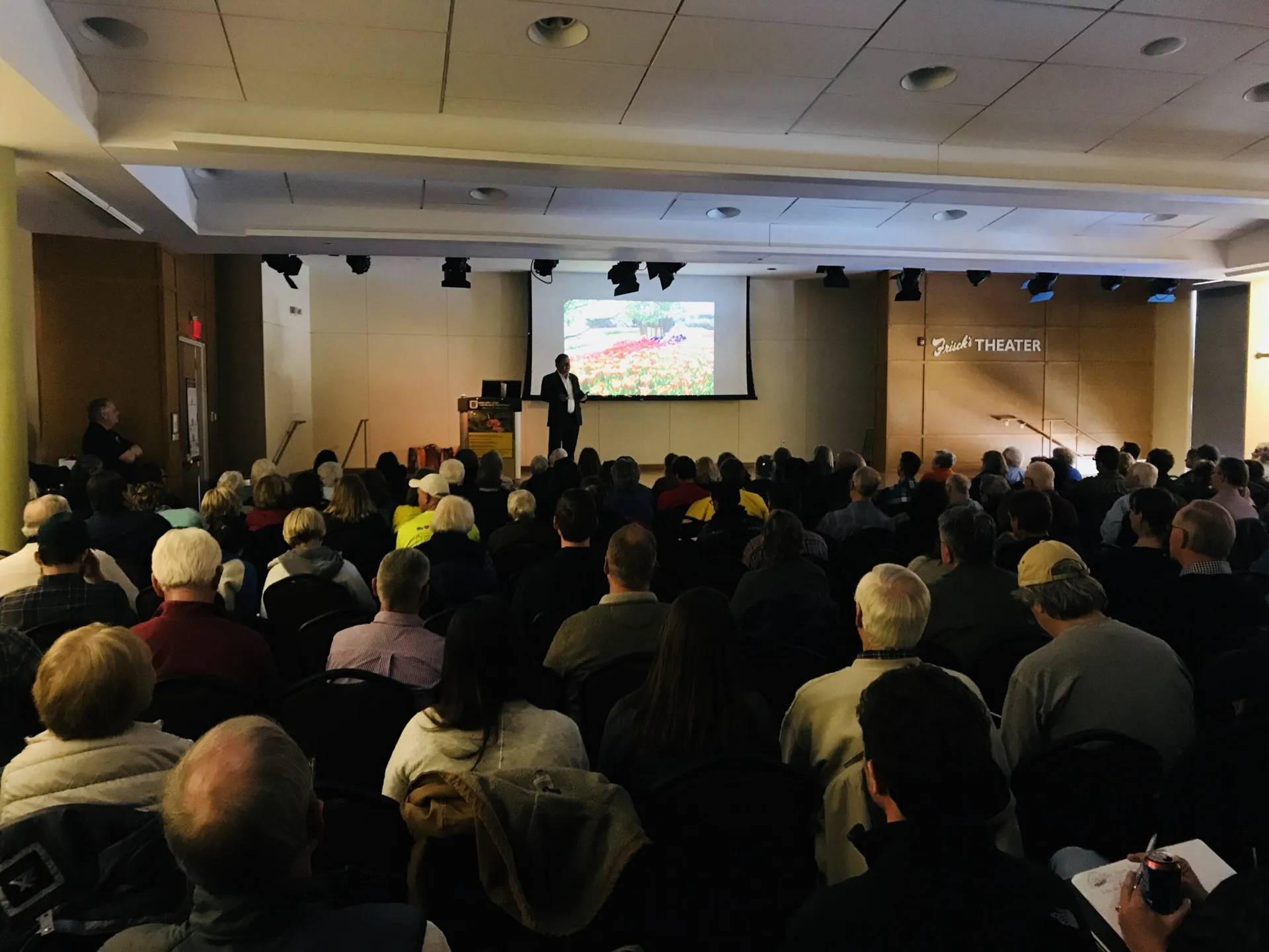 person speaking in a full room at a garden symposium